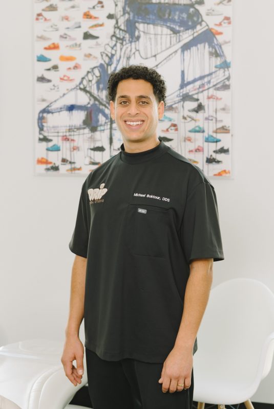 Portrait of Dr. Michael Boktour in black scrubs smiling in front of artwork featuring a large sneaker graphic with paint drips.