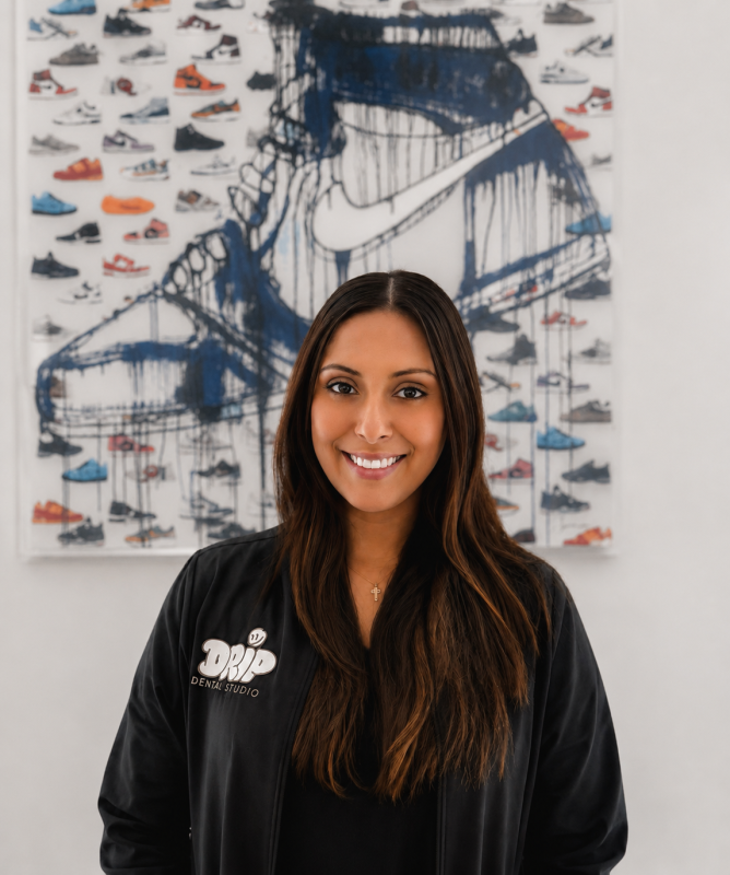 Headshot of Victoria Office Manager wearing a black Drip Dental Studio jacket, smiling in front of sneaker-themed artwork.